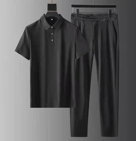 Ensemble d’été pour homme noir composé d’un polo à manches courtes et d’un pantalon léger à taille élastique, suspendu sur cintres sur fond gris.