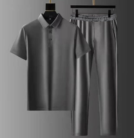 Ensemble d’été pour homme gris composé d’un polo à manches courtes et d’un pantalon léger à taille élastique, suspendu sur cintres sur fond gris.