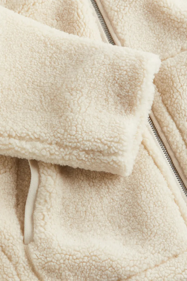 Gros plan sur la manche d'une veste teddy blanche, révélant la texture douce et moelleuse du tissu. Les poignets sont finis dans un tissu beige assorti, pour un style soigné et confortable.