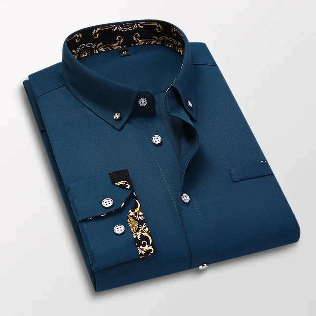 Chemise longue Bruno pour homme bleu pétrole, col pointu et manches longues, pliée avec boutons contrastés et détails imprimés au col et aux poignets.