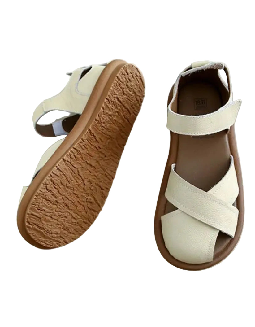 Une paire de sandales plates pour femmes au design moderne, avec des brides croisées en cuir beige clair et une semelle en caoutchouc souple de couleur marron. Ces sandales sont parfaites pour l'été, alliant confort et style.