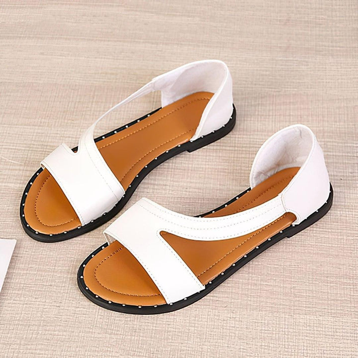 Sandales plates femme Capucine tendance blanches, bout ouvert, bride large asymétrique avec découpes, semelle camel et contour clouté, présentées en vue de dessus sur fond clair.