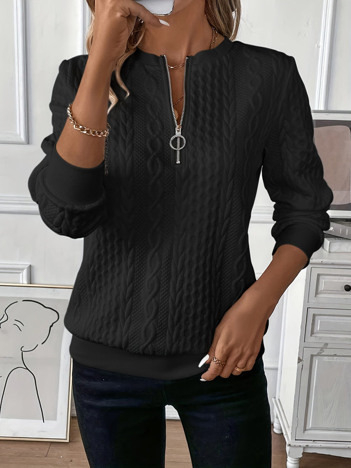 Femme portant un pull noir texturé à motifs torsadés avec une fermeture éclair argentée sur le devant. Le vêtement, à manches longues et à coupe ajustée, allie élégance et modernité, idéal pour un look chic et décontracté.