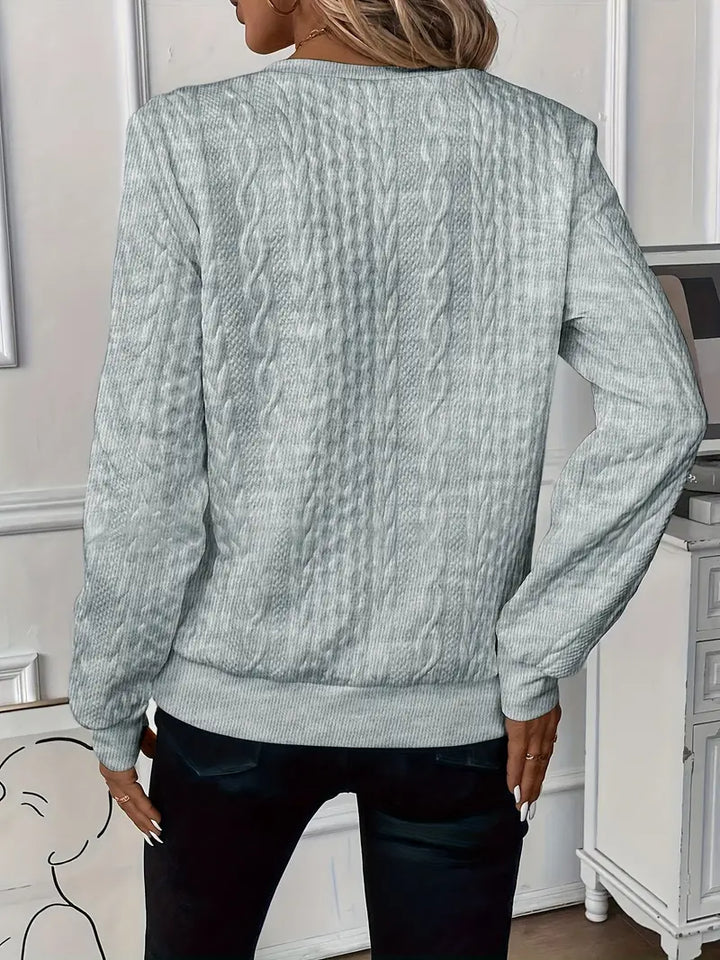 Vue de dos d'une femme portant un pull gris texturé à torsades verticales. Ce vêtement à manches longues et à coupe droite présente des finitions côtelées aux poignets et à l'ourlet, offrant un style moderne et raffiné, idéal pour la saison fraîche.