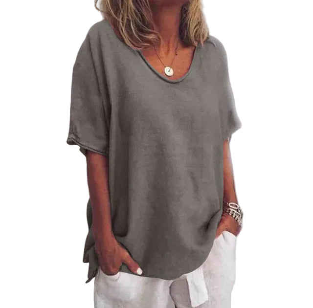 Blouse ample pour femme Cécile gris uni, coupe décontractée à col rond et manches courtes, portée avec un pantalon blanc et des bracelets.