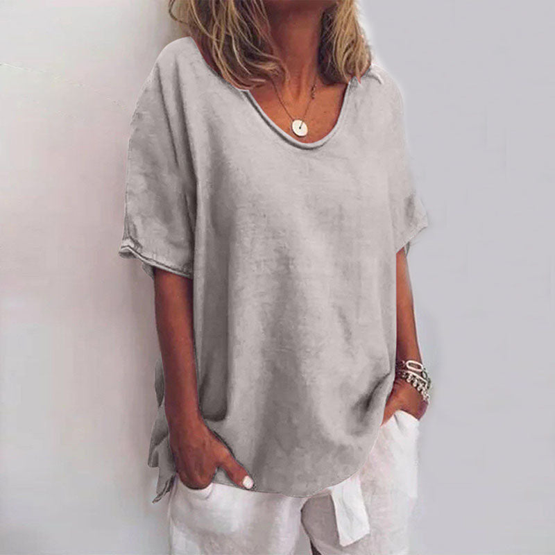 Blouse ample pour femme Cécile gris clair uni, coupe décontractée à col rond et manches courtes, portée avec un pantalon blanc et des bracelets.