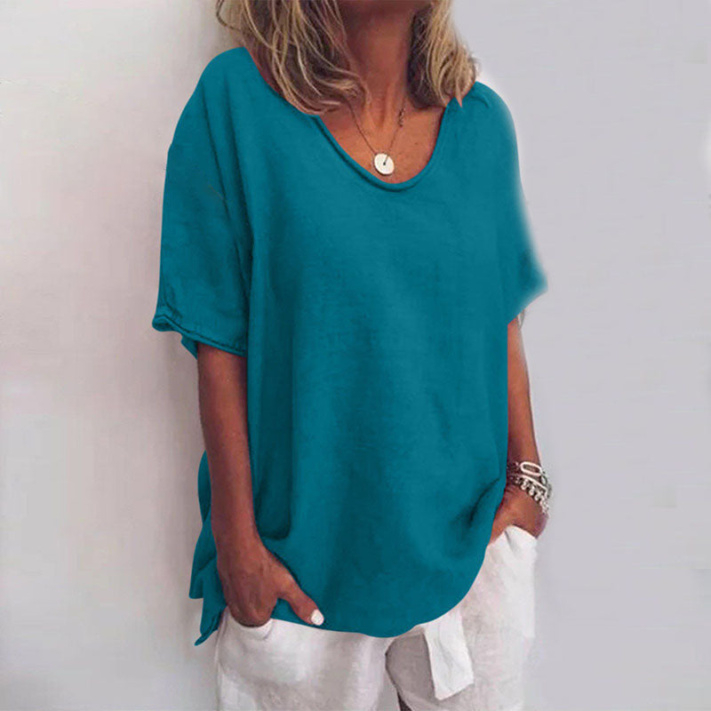 Blouse ample pour femme Cécile bleu pétrole unie, coupe décontractée à col rond et manches courtes, portée avec un pantalon clair et des bracelets.