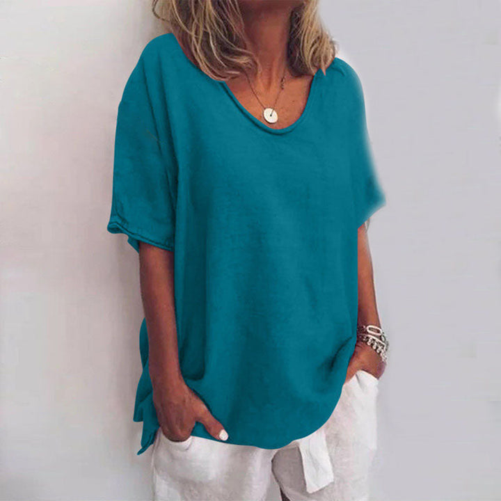 Blouse ample pour femme Cécile bleu pétrole unie, coupe décontractée à col rond et manches courtes, portée avec un pantalon clair et des bracelets.