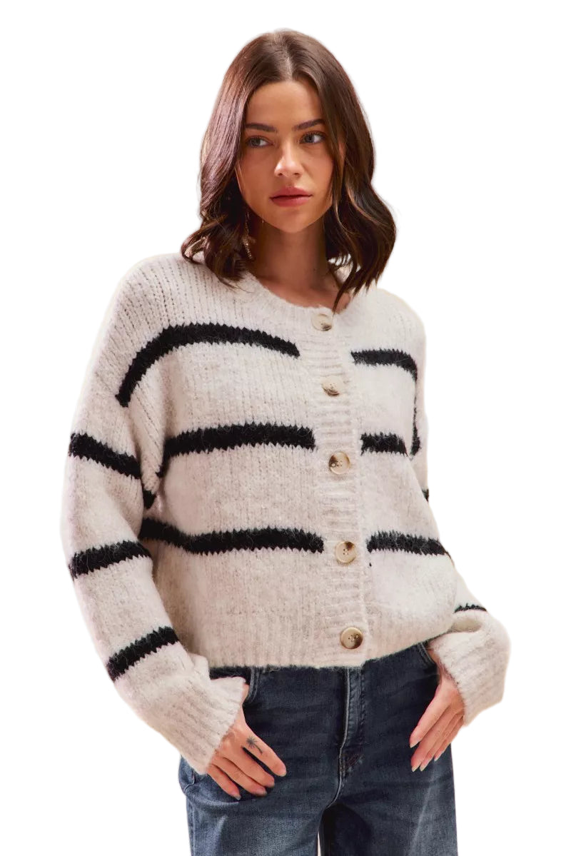 Le mannequin porte un cardigan en maille douce à boutons, col rond, de couleur blanche à rayures noires, coupe décontractée, manches longues, associé à un jean.