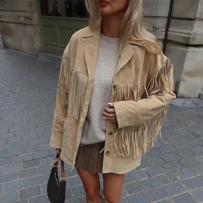 "Veste à franges pour femme, modèle Charlène. Veste beige à franges portée avec un pull beige et un short marron, parfaite pour un look tendance et décontracté. Accessoirisée avec un sac à main noir pour une touche élégante.