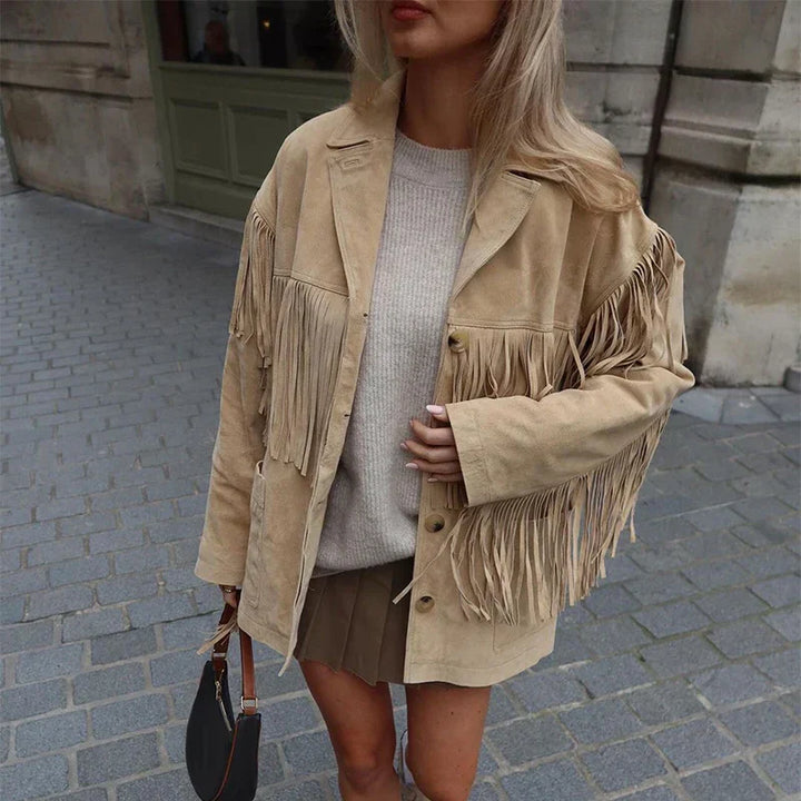 "Veste à franges pour femme, modèle Charlène. Veste beige à franges portée avec un pull beige et un short marron, parfaite pour un look tendance et décontracté. Accessoirisée avec un sac à main noir pour une touche élégante.