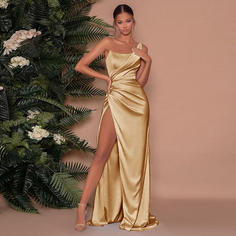 Femme portant une robe longue en satin doré, à une épaule, avec une fente haute sur la cuisse. La tenue élégante épouse la silhouette et reflète la lumière pour un effet luxueux. Le look est complété par des sandales à talons fins, parfait pour une soirée chic ou un événement formel.