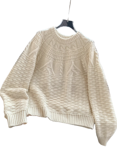 Un pull blanc en maille épaisse, à col rond et à motifs texturés, présenté sur un cintre et posé sur une chaise de bureau dans un intérieur moderne.