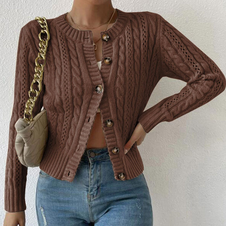 Femme portant un cardigan en maille torsadée marron, légèrement ouvert sur un haut clair, assorti à un jean taille haute et accompagné d’un sac à chaîne dorée.