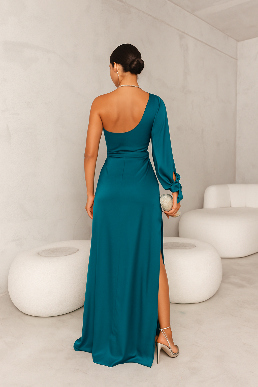 Vue arrière de cette élégante robe bleu-vert satinée avec une coupe asymétrique à épaule unique et un détail noué à la taille. La fente latérale ajoute un effet sensuel, tandis que le sac à main argenté et les talons assortis complètent cette tenue chic et moderne, parfaite pour vos événements spéciaux.