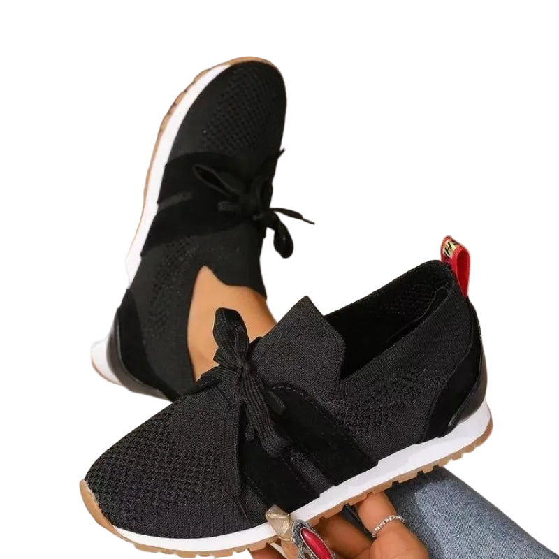 Modernes, sneakers noires en maille avec lacets et semelle blanche, portées et tenues à la main en intérieur.