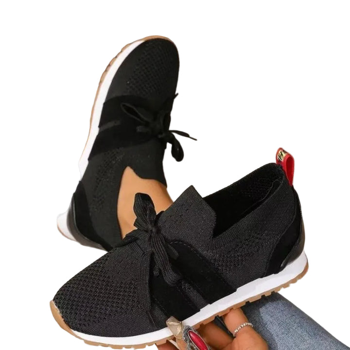 Modernes, sneakers noires en maille avec lacets et semelle blanche, portées et tenues à la main en intérieur.