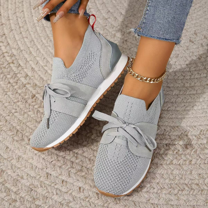Modernes, sneakers grises en maille avec bande et lacets, semelle blanche et gomme, portées avec un jean sur tapis.