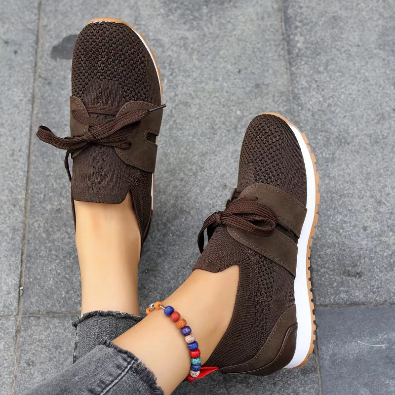Modernes, sneakers marron en maille avec bande et lacets, semelle blanche et gomme, portées sur sol en pierre.