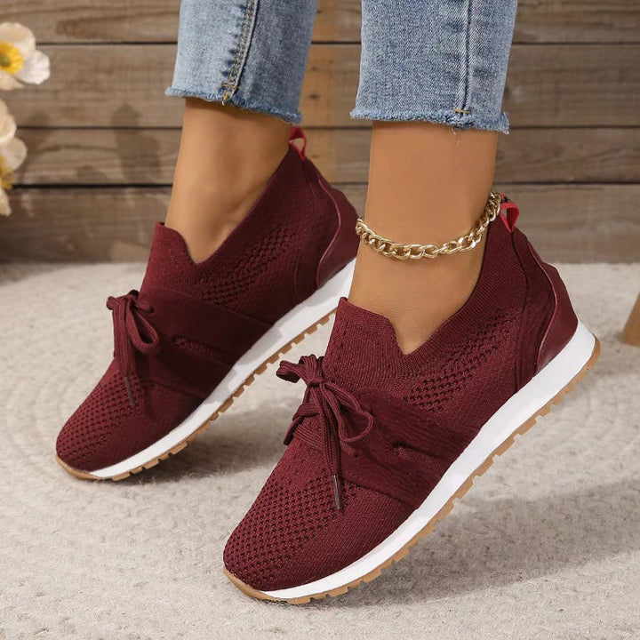 Modernes, sneakers bordeaux en maille avec bande et lacets, semelle blanche et gomme, portées avec un jean en intérieur.