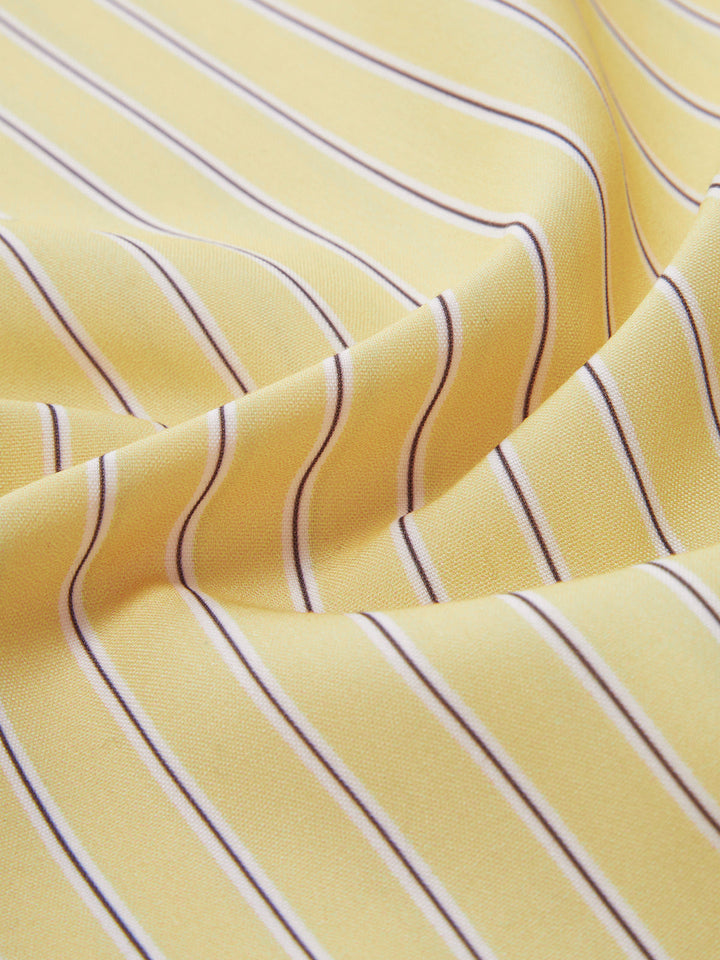 Zoom sur le tissu de la chemise rayée jaune et blanche. Les rayures fines et régulières créent un motif élégant et moderne, mettant en valeur la douceur et la texture du tissu, parfait pour une tenue estivale stylée.
