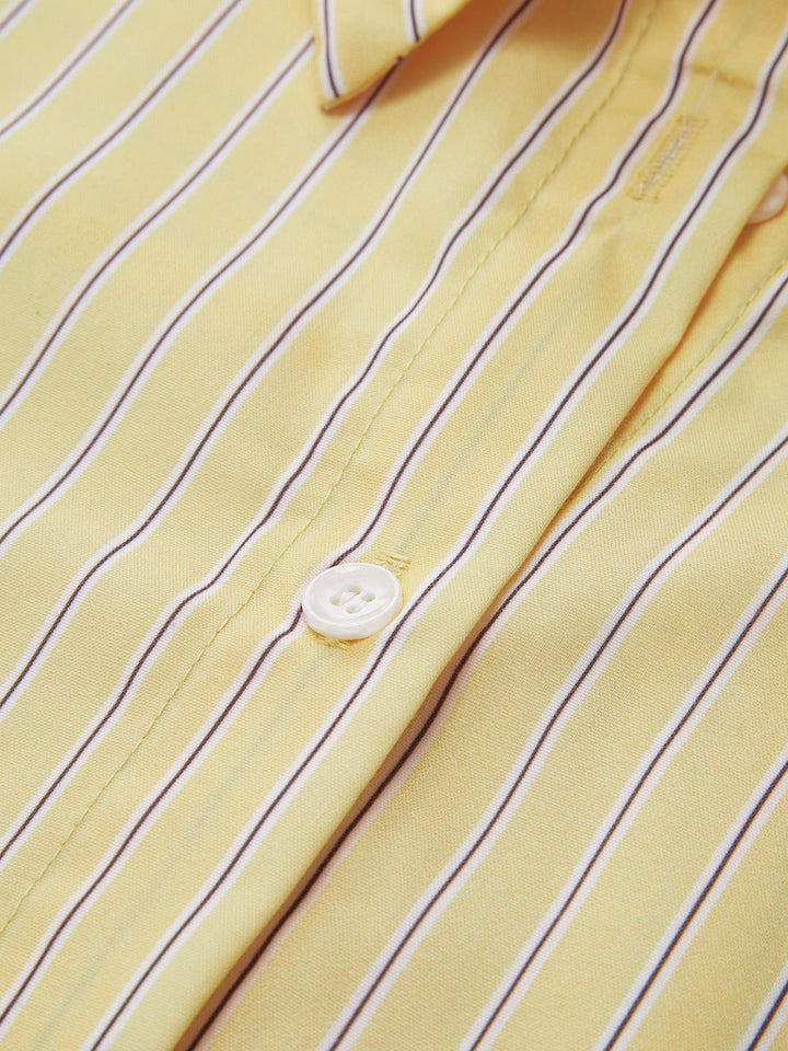 Zoom sur les boutons de la chemise rayée jaune et blanche. Les rayures fines et régulières apportent une touche élégante et moderne à cette chemise, tandis que le bouton blanc classique complète le look.