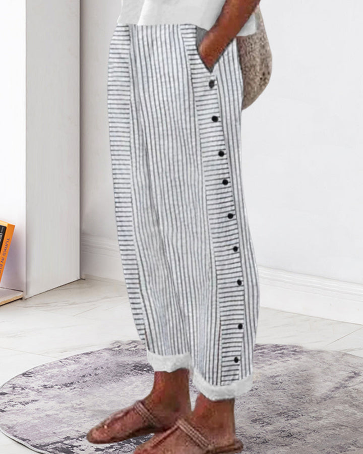 Jogging décontracté femme à rayures gris et blanc, coupe ample avec taille élastique, poches et boutons décoratifs sur le côté, porté avec des chaussures plates style moderne et confortable.