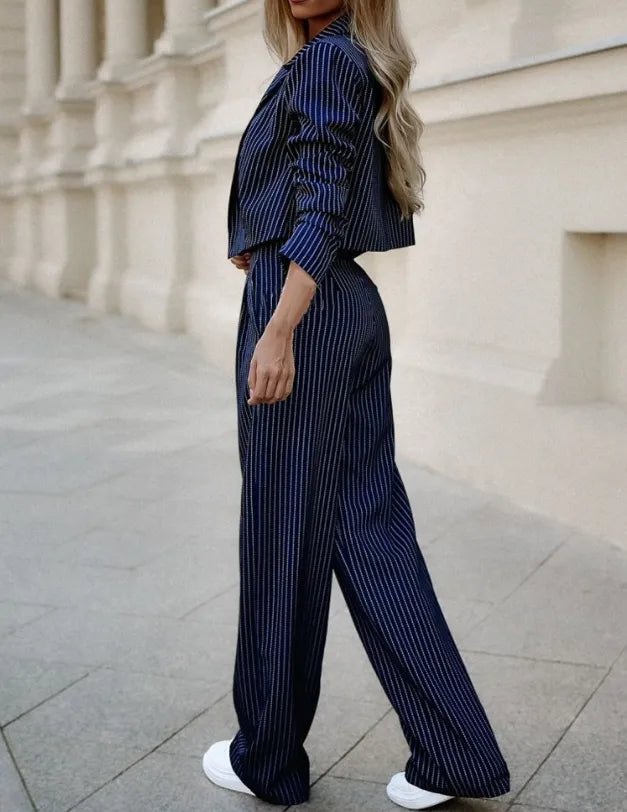 Ensemble pour femme Doriane tendance, vue de profil, costume bleu marine à fines rayures avec blazer court et pantalon large, porté avec des baskets blanches.