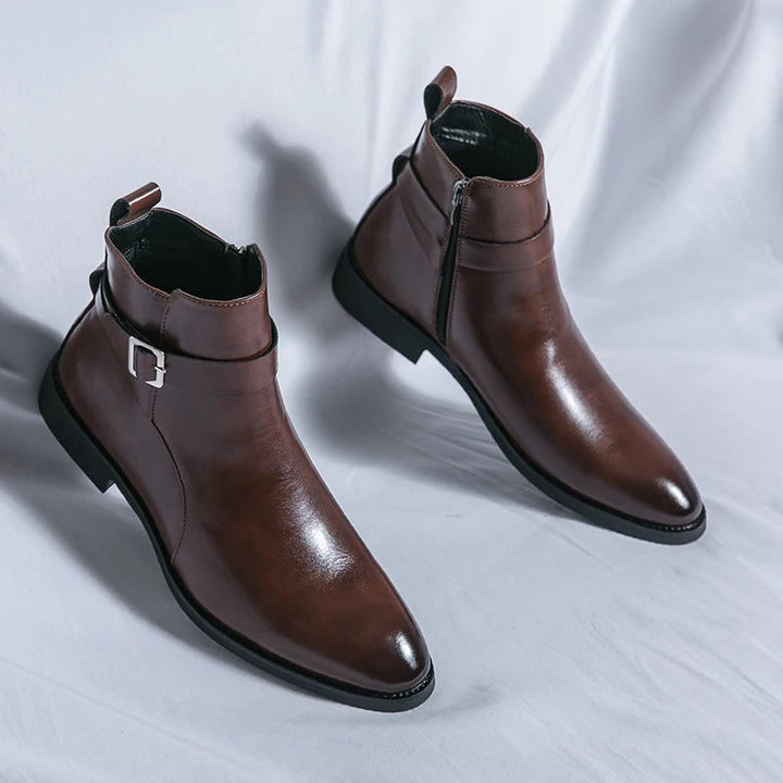 Paire de bottines cheville marron en cuir lisse, bout légèrement effilé, fermeture éclair latérale et bride avec boucle, posées sur fond clair.