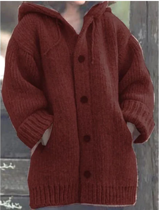 Femme portant un long cardigan rouge en maille épaisse, à capuche, à manches larges et à gros boutons assortis, offrant un look douillet et chaud, idéal pour l'hiver.