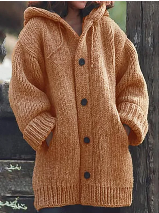 Femme portant un long gilet orange en grosse maille, à capuche, à manches larges et à gros boutons foncés, offrant un style chaud et confortable, idéal pour l'hiver.