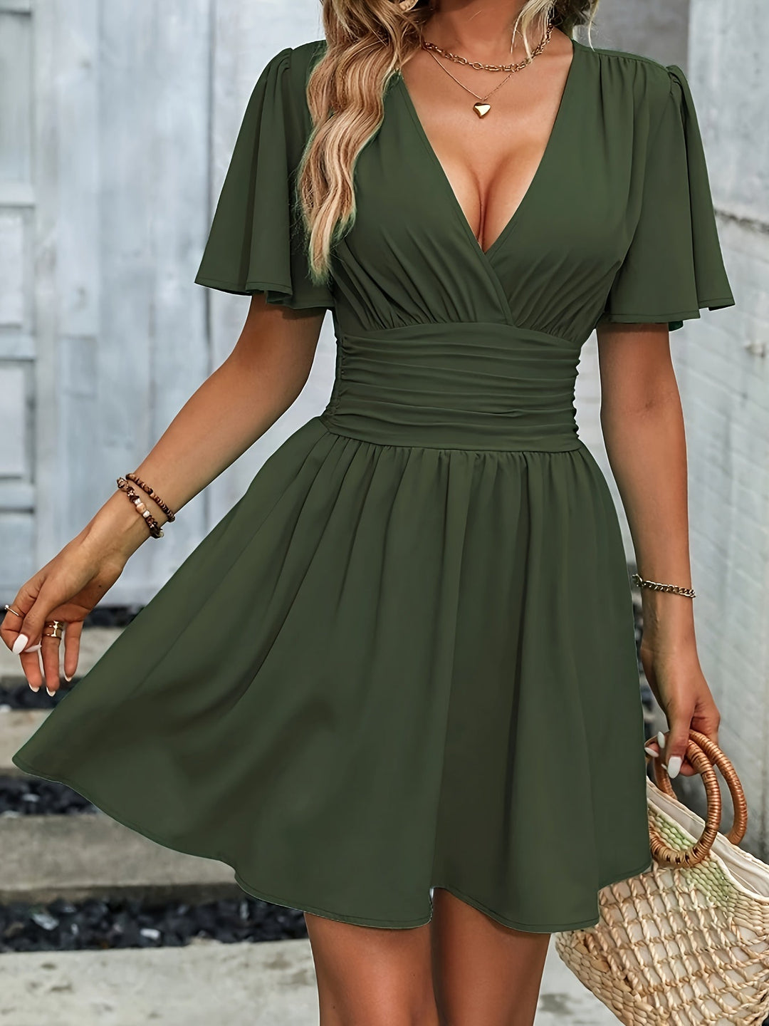Robe col V pour femme Elowen tendance, couleur vert kaki, taille froncée et jupe évasée, manches courtes fluides, portée avec un sac en paille.