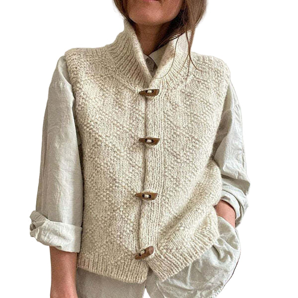 Femme portant un gilet en maille texturée de couleur blanche, fermé par quatre boutons en bois, superposé à une chemise ample à manches retroussées.