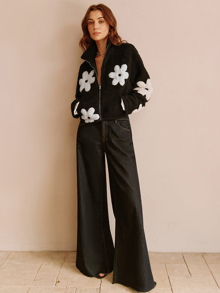 Adoptez un look moderne et tendance avec cette veste courte en fausse fourrure noire, ornée de fleurs blanches. Associez-la à un pantalon large pour une tenue à la fois décontractée et chic. Parfaite pour un style urbain et confortable.