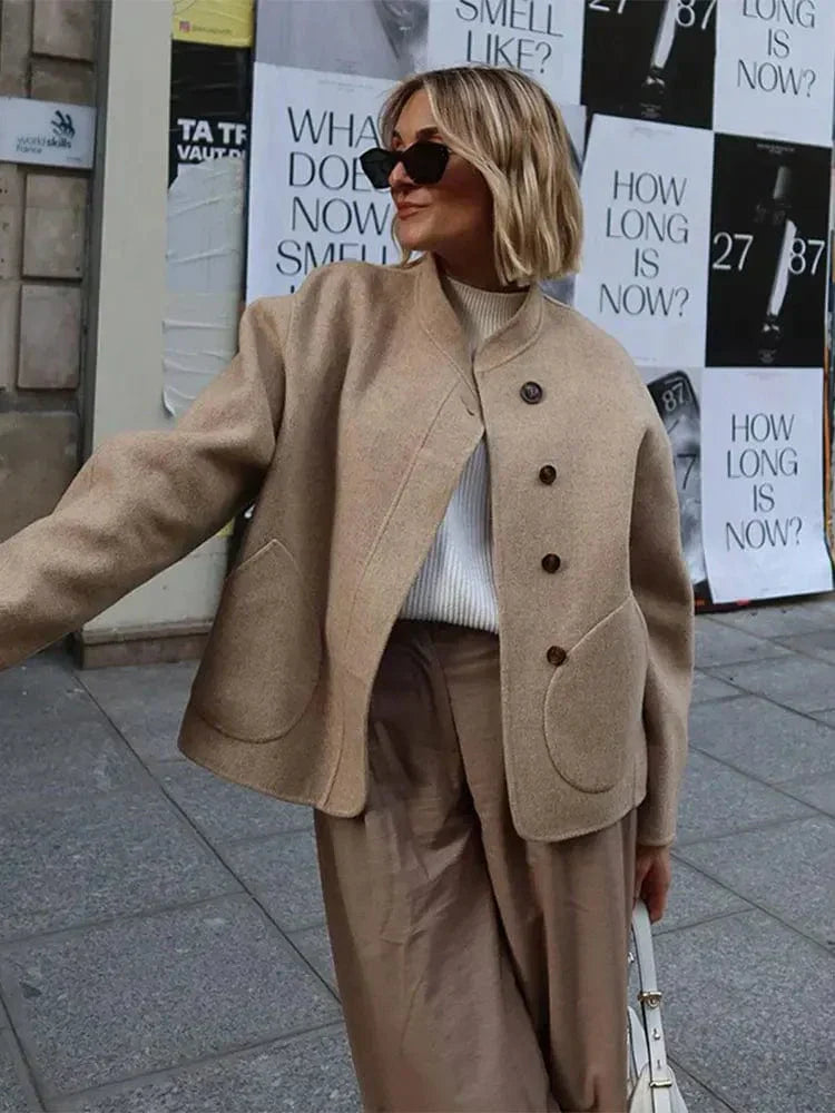 Veste courte pour femme Ethelyn, parfaite pour l'hiver. Ce modèle beige avec des boutons en bois et des poches arrondies offre un look à la fois élégant et décontracté. Idéale pour un style chic et cosy, cette veste se porte facilement avec un pull doux et un pantalon fluide, ajoutant une touche de sophistication à vos tenues hivernales.