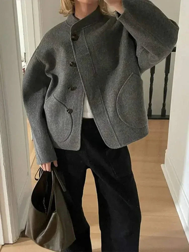 Veste courte pour femme Ethelyn en gris, avec des boutons en bois et des poches arrondies pour une touche moderne. Son design élégant et confortable est idéal pour l'hiver. Cette veste se marie parfaitement avec un pull chaud et un pantalon large, créant une silhouette chic et décontractée, tout en apportant chaleur et style.