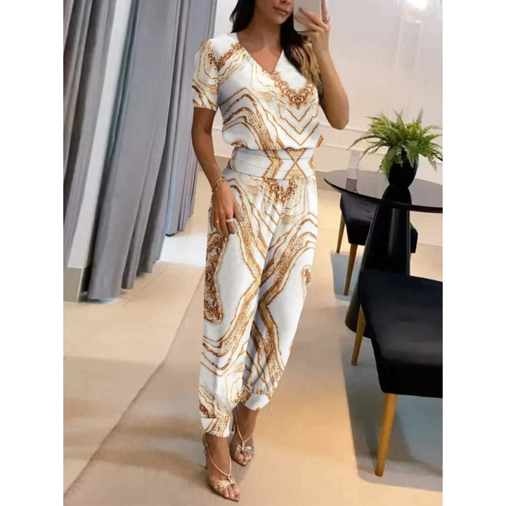 Ensemble chic pour femme Eugénie, moderne et élégant, de couleur blanche avec des motifs géométriques dorés. Cet ensemble fluide, composé d'un haut à col en V et d'un pantalon assorti à bords côtelés, offre un look raffiné et sophistiqué, parfait pour une occasion spéciale ou un style quotidien stylé.