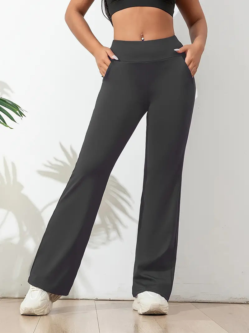 Femme portant un pantalon de yoga gris avec une taille haute et des poches latérales, combiné avec un crop top noir et des baskets blanches, en pose décontractée.