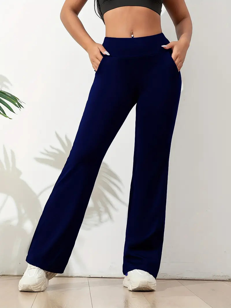 Femme portant un pantalon de yoga bleu marine avec une taille haute et des poches latérales, associé à un crop top noir et des baskets blanches, posant dans une position décontractée.