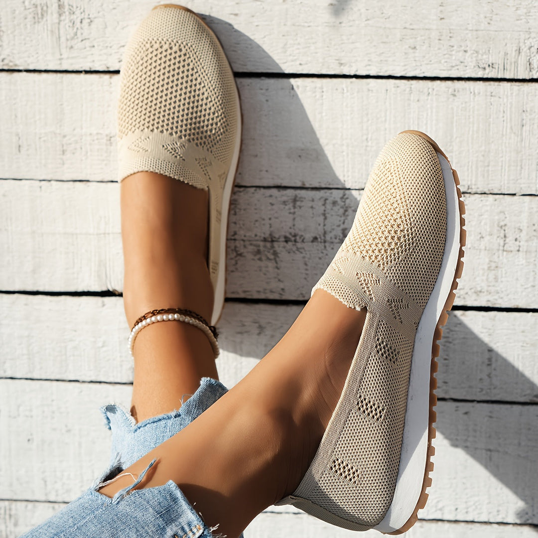Chaussures d’été femme Fantine tendance beige portées aux pieds, slip-on en maille ajourée respirante, bout arrondi et semelle blanche avec dessous cranté, vue de dessus sur fond bois clair.