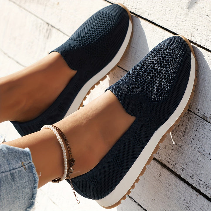 Chaussures d’été femme Fantine tendance bleu marine, slip-on en maille respirante, bout arrondi et semelle blanche légère avec dessous cranté, portées en extérieur sur fond bois clair.