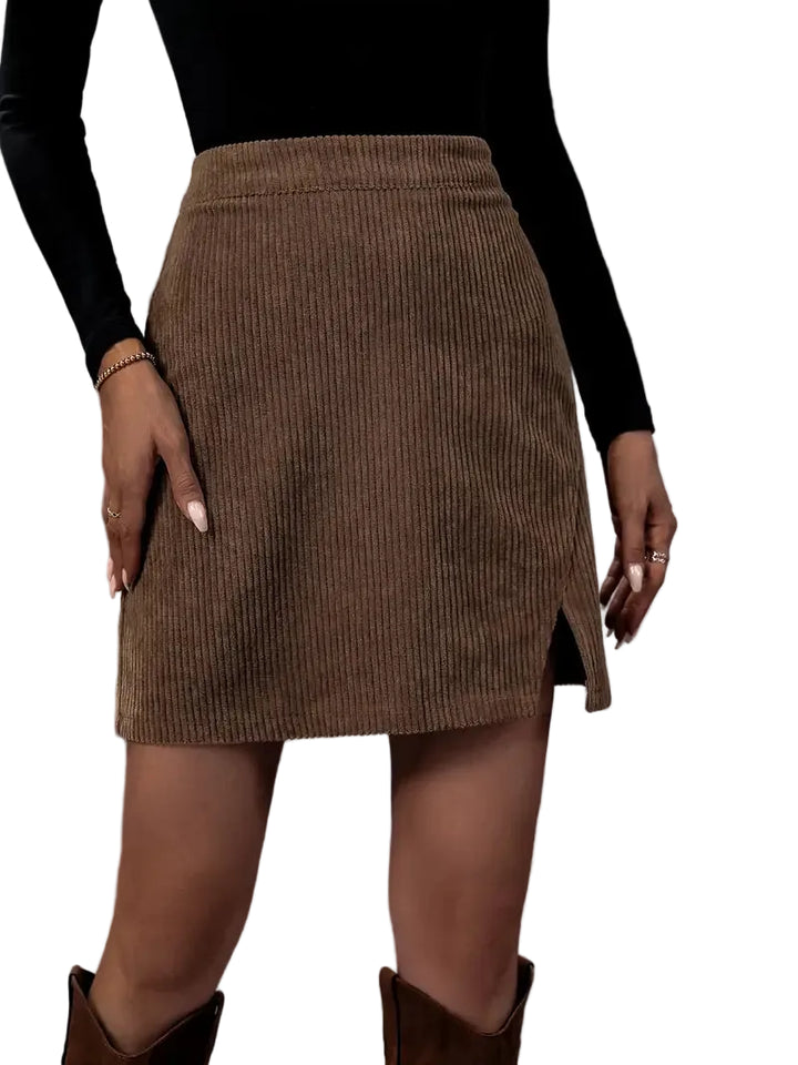 Mini-jupe en velours côtelé marron pour femme, coupe moderne ajustée avec fente discrète, portée avec un haut noir à manches longues et un sac à main, look chic et contemporain.