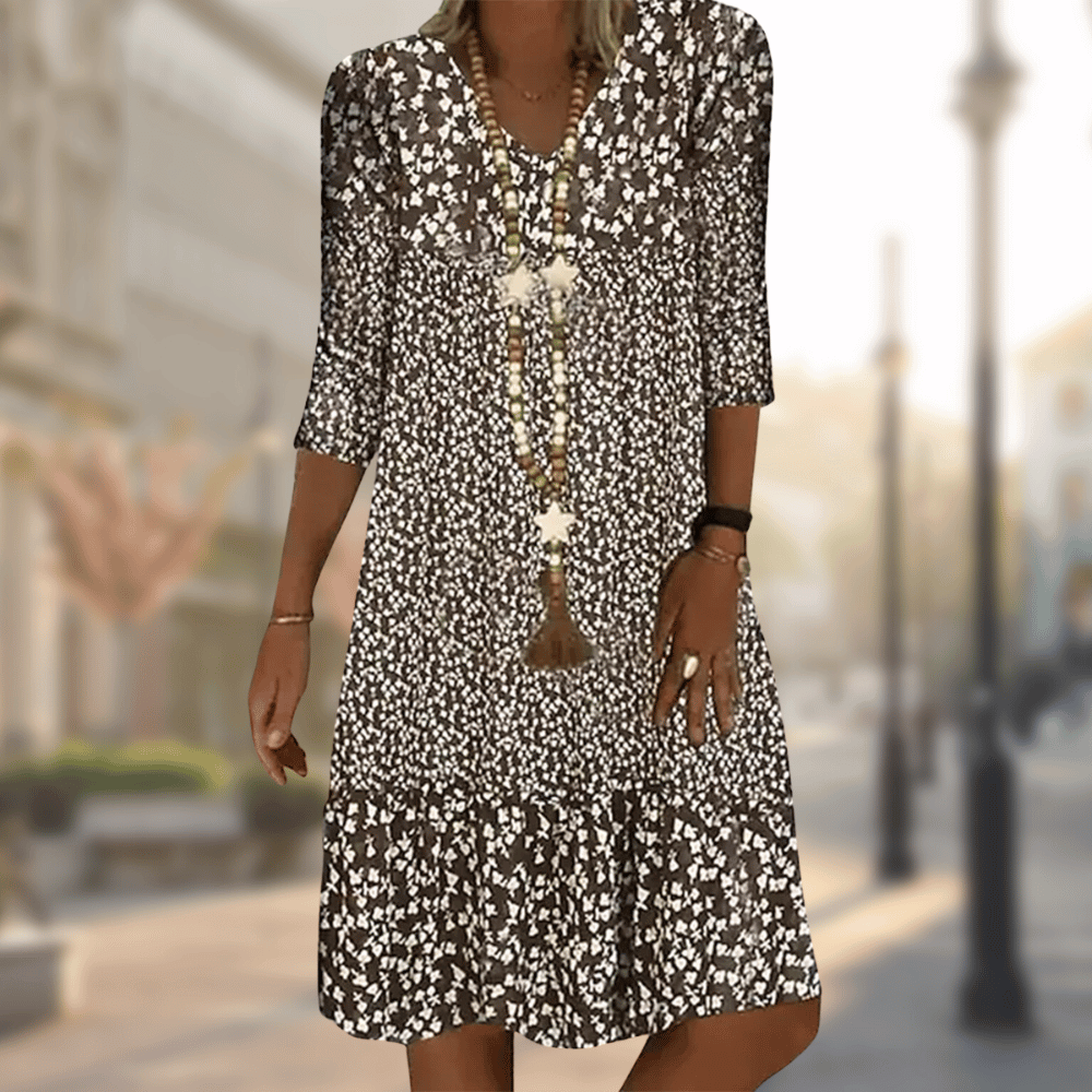 Robe midi femme Faustine moderne à imprimé floral noir et blanc, manches 3/4 et col en V, coupe fluide avec bas volanté, portée avec un long collier, en extérieur.
