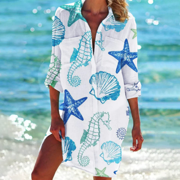 robe-chemise légère blanche à manches 3/4 avec col ouvert, imprimé marin étoiles de mer, coquillages et hippocampes bleus et verts, coupe fluide idéale pour un look estival en bord de mer.