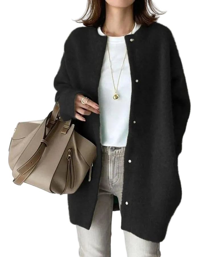 Femme portant un cardigan long noir à coupe droite, avec boutons sur le devant et texture douce et chaude, porté sur un haut blanc et un jean clair, complété par un sac à main beige et des bijoux discrets, dans un style élégant et minimaliste.