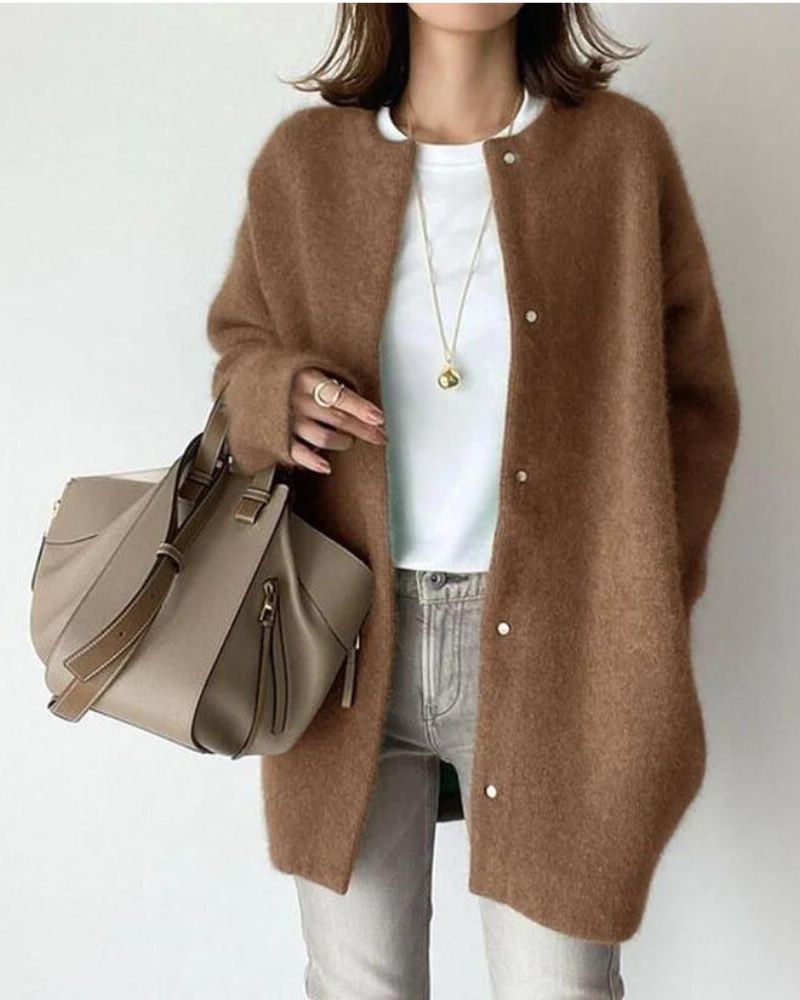 Femme portant un cardigan long couleur camel à coupe droite, avec boutons sur le devant et texture douce et chaude, porté sur un haut blanc et un jean clair, accessoirisé d’un sac à main beige et de bijoux discrets, dans un style élégant et intemporel.