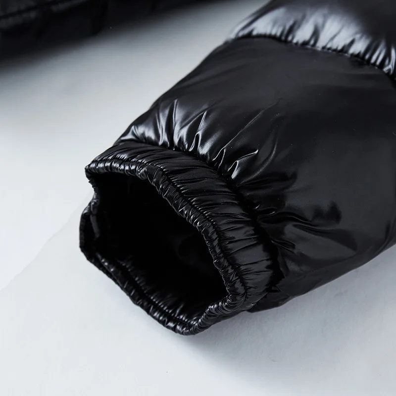 Vue rapprochée de la manche d'une doudoune noire brillante, mettant en évidence le tissu matelassé et l'élastique au niveau du poignet pour un ajustement confortable et isolant.