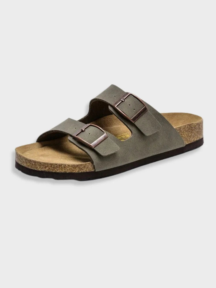 Sandales d'été pour femme, dotées de deux larges brides en cuir gris foncé et de boucles métalliques réglables. La semelle intérieure en liège et latex épouse la forme du pied pour un confort optimal, tandis que la semelle extérieure antidérapante assure une démarche stable. Leur design sobre et moderne en fait le choix idéal pour un look décontracté en été.