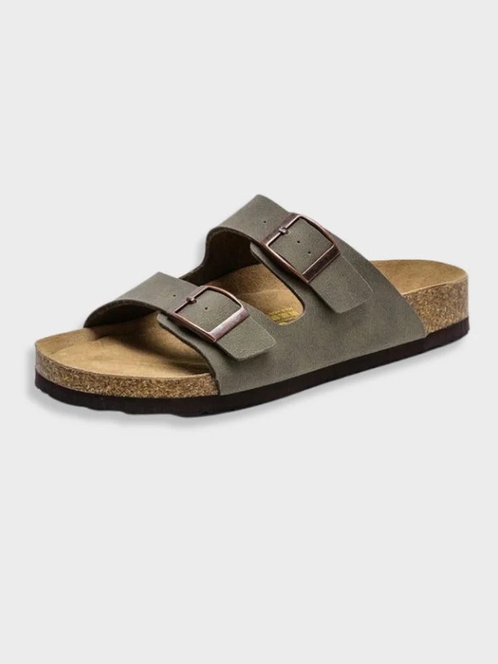 Sandales d'été pour femme, dotées de deux larges brides en cuir gris foncé et de boucles métalliques réglables. La semelle intérieure en liège et latex épouse la forme du pied pour un confort optimal, tandis que la semelle extérieure antidérapante assure une démarche stable. Leur design sobre et moderne en fait le choix idéal pour un look décontracté en été.