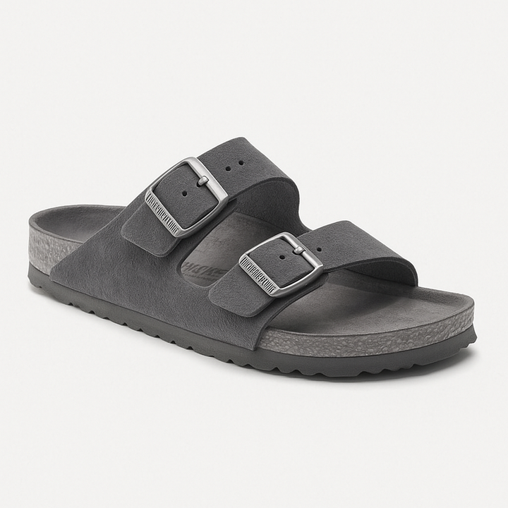 Sandales d'été à deux brides en cuir gris et boucles métalliques réglables. La semelle ergonomique en liège et latex offre un excellent maintien et un confort durable. Leur design minimaliste et moderne est idéal pour un style décontracté lors des chaudes journées d'été.